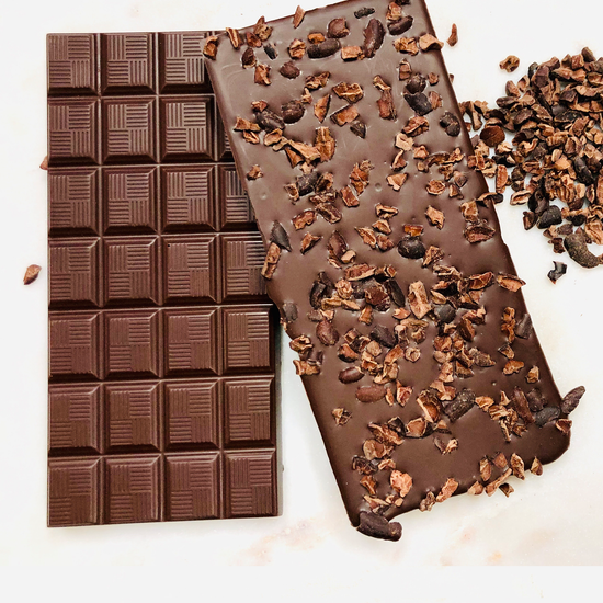 Two bars of dark chocolate, one front-image and one back image of bar scattered with cacao nibs on a white background.