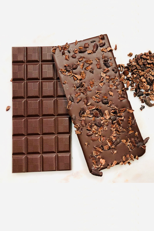 Two bars of dark chocolate, one front-image and one back image of bar scattered with cacao nibs on a white background.