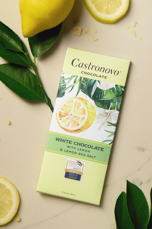 A bar of Castronovo white chocolate with lemon and lemon sea salt, presented on a marble surface with lemon slices and green leaves in the background.