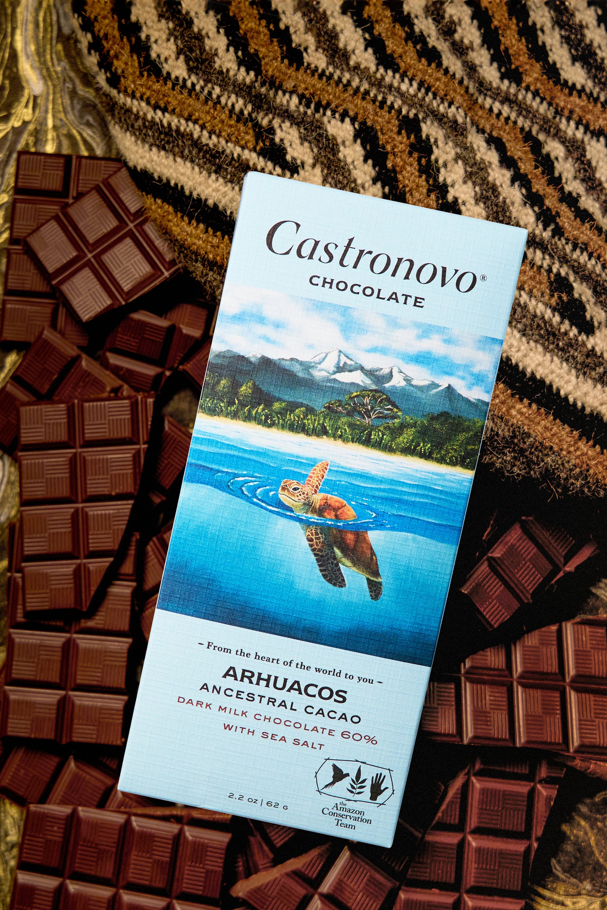 A bar of Castronovo chocolate with a turtle on the packaging, surrounded by multiple pieces of chocolate on a patterned surface.