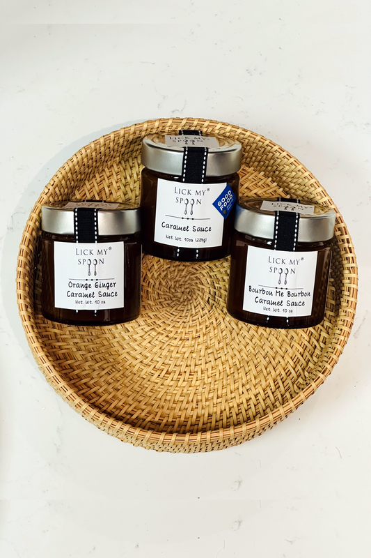 Three jars of "Lick My Spoon" brand caramel sauce displayed side-by-side inside a woven basket
