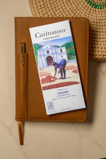 A bar of Castronovo Venezuela 72% Dark chocolate placed on top of a brown notebook with an illustration of a person on the cover, set on a kitchen counter.