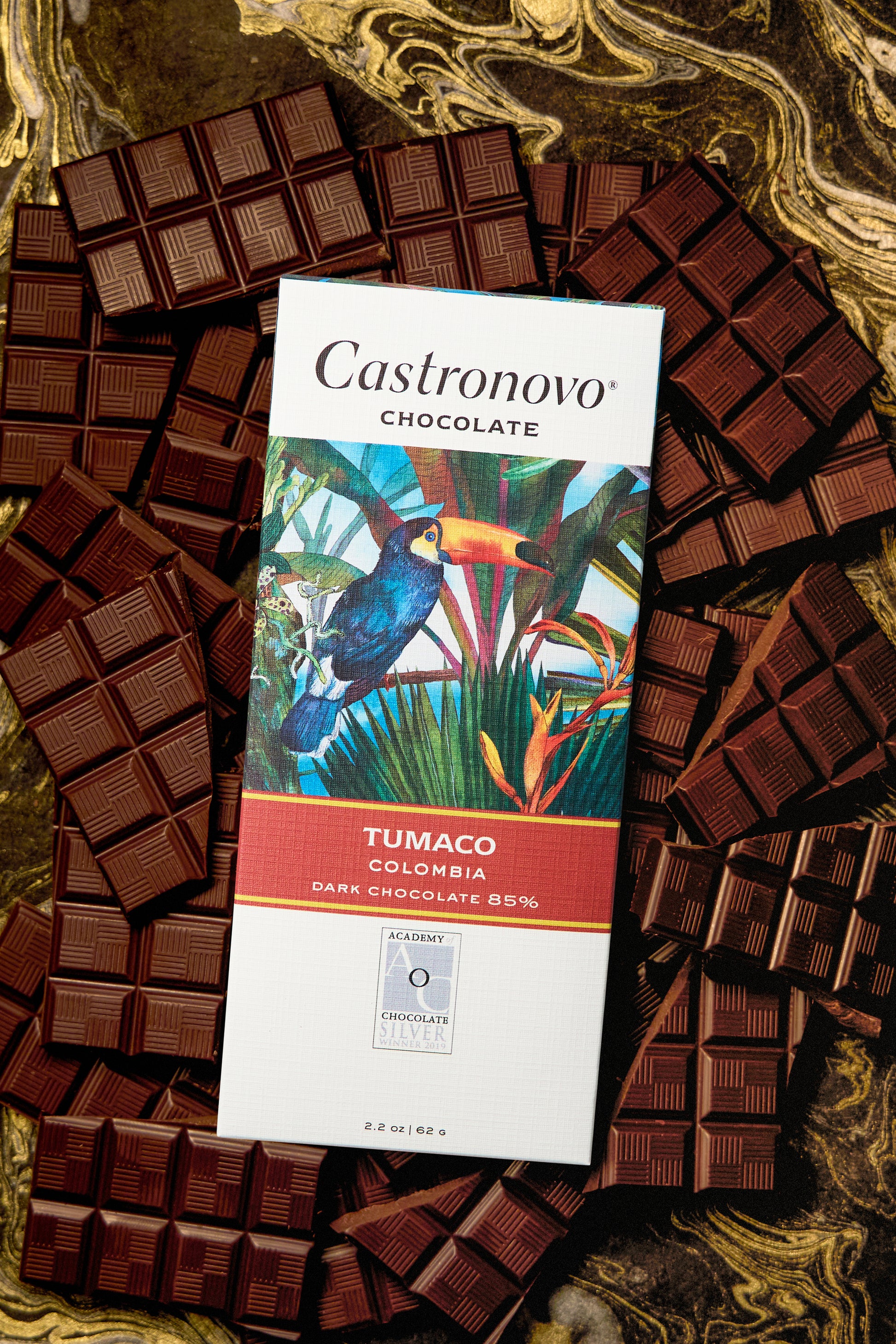 A bar of Castronovo chocolate with 'TUMACO COLOMBIA' text and an image of a bird on it, surrounded by multiple pieces of dark chocolate.