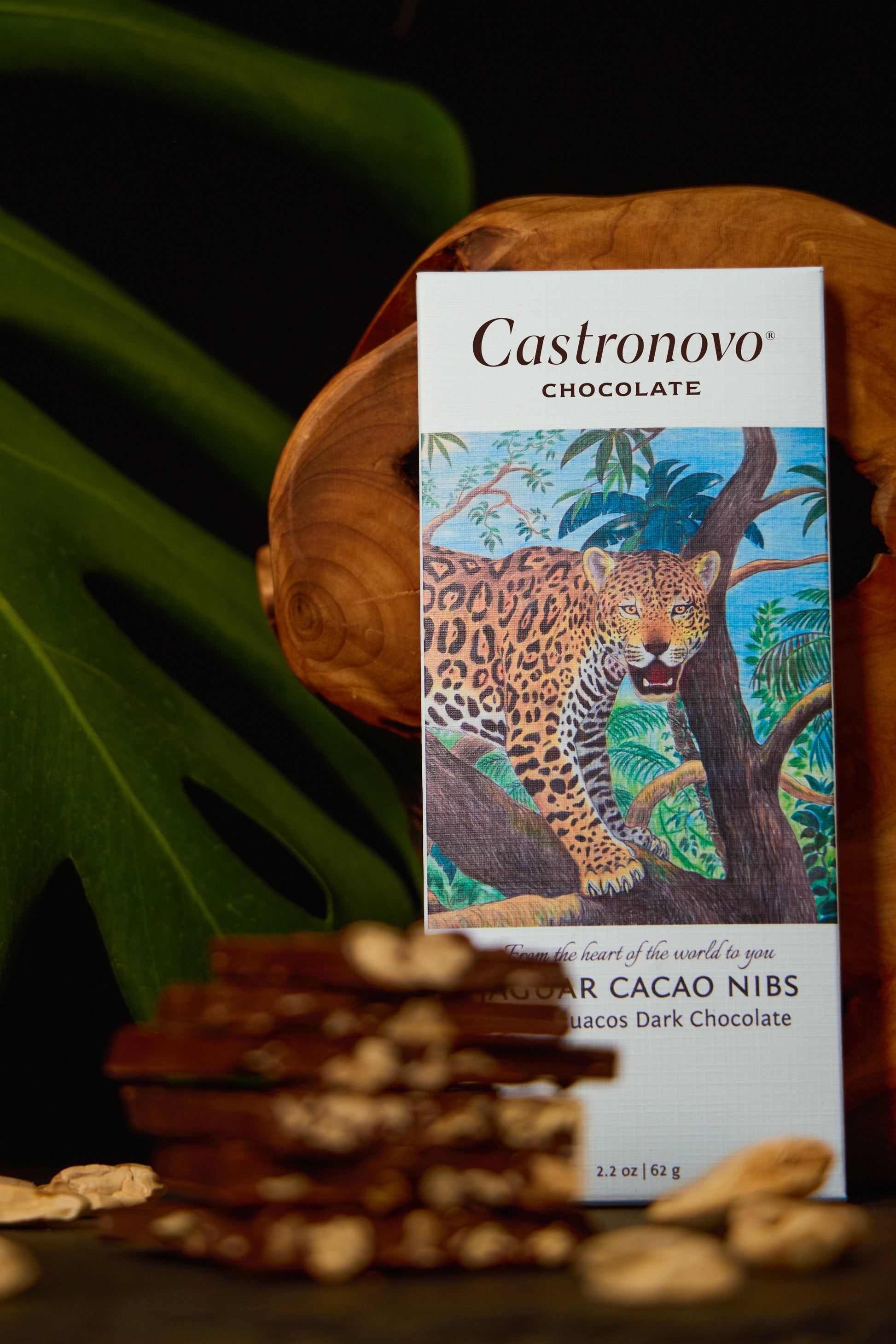 A bar of Castronovo chocolate with a jaguar on the packaging, displayed alongside jaguar cacao nibs on a wooden surface.