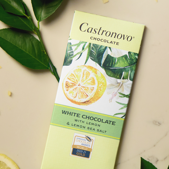 A bar of Castronovo white chocolate with lemon and lemon sea salt, presented on a marble surface with lemon slices and green leaves in the background.
