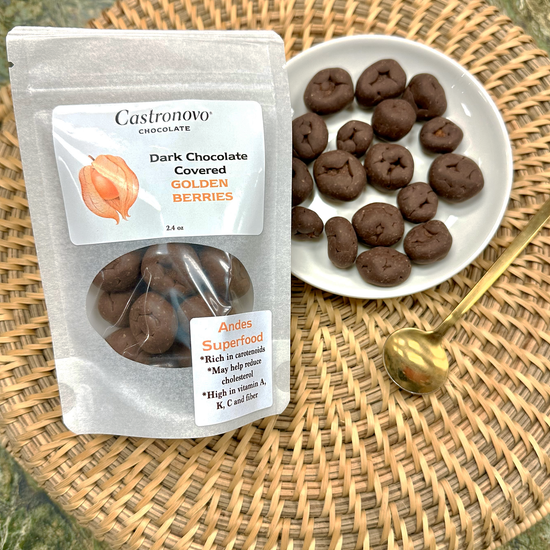A clear plastic package with dark chocolate covered golden berries next to a white plate with the same berries. The package has a label indicating 'Dark Chocolate Covered Golden Berries' and the brand 'Castronovo'.