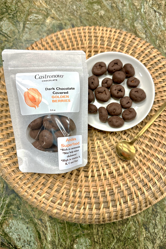 A clear plastic package with dark chocolate covered golden berries next to a white plate with the same berries. The package has a label indicating 'Dark Chocolate Covered Golden Berries' and the brand 'Castronovo'.