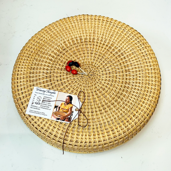 A round, woven basket made of natural materials by the women of the Piaroa indigenous group, with a tag attached displaying a picture and information about the product.