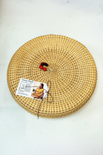 A round, woven basket made of natural materials by the women of the Piaroa indigenous group, with a tag attached displaying a picture and information about the product.