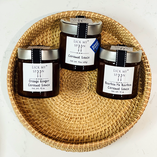 Three jars of "Lick My Spoon" brand caramel sauce displayed side-by-side inside a woven basket 