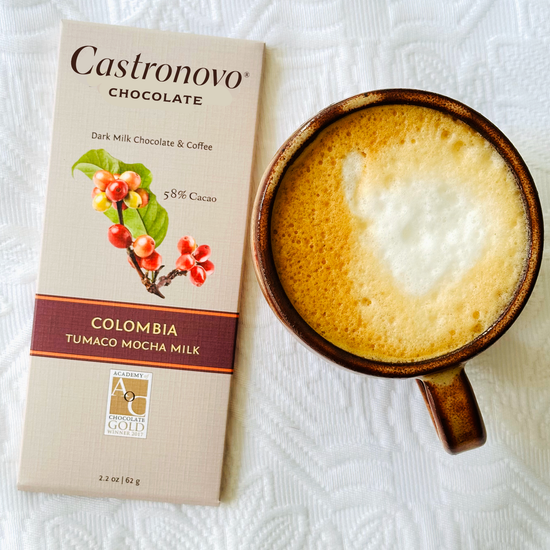 A bar of Castronovo chocolate with 'Colombia' text and a picture of a flower, alongside a steaming cup of mocha on a white surface.