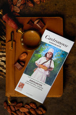 A bar of Arhuacos 80% dark chocolate by Castronovo Chocolate, placed on a surface with cocoa beans and a magnifying glass.