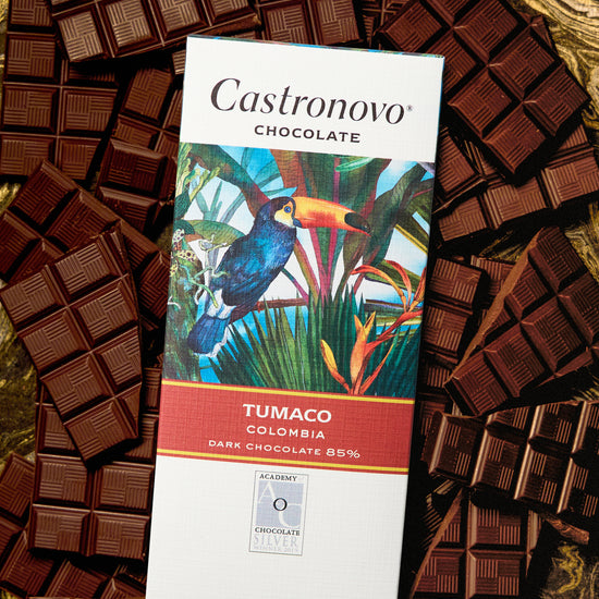 A bar of Castronovo chocolate with 'TUMACO COLOMBIA' text and an image of a bird on it, surrounded by multiple pieces of dark chocolate.