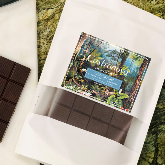 A chocolate chef tablet with a label showing the brand and possibly the Peruvian Amazonian landscape. The tablet is placed on a white paper, which is on a textured background.