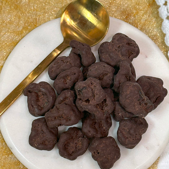 A plate of dark chocolate covered Montmorency cherries with a golden spoon on the side, placed on a yellow napkin.